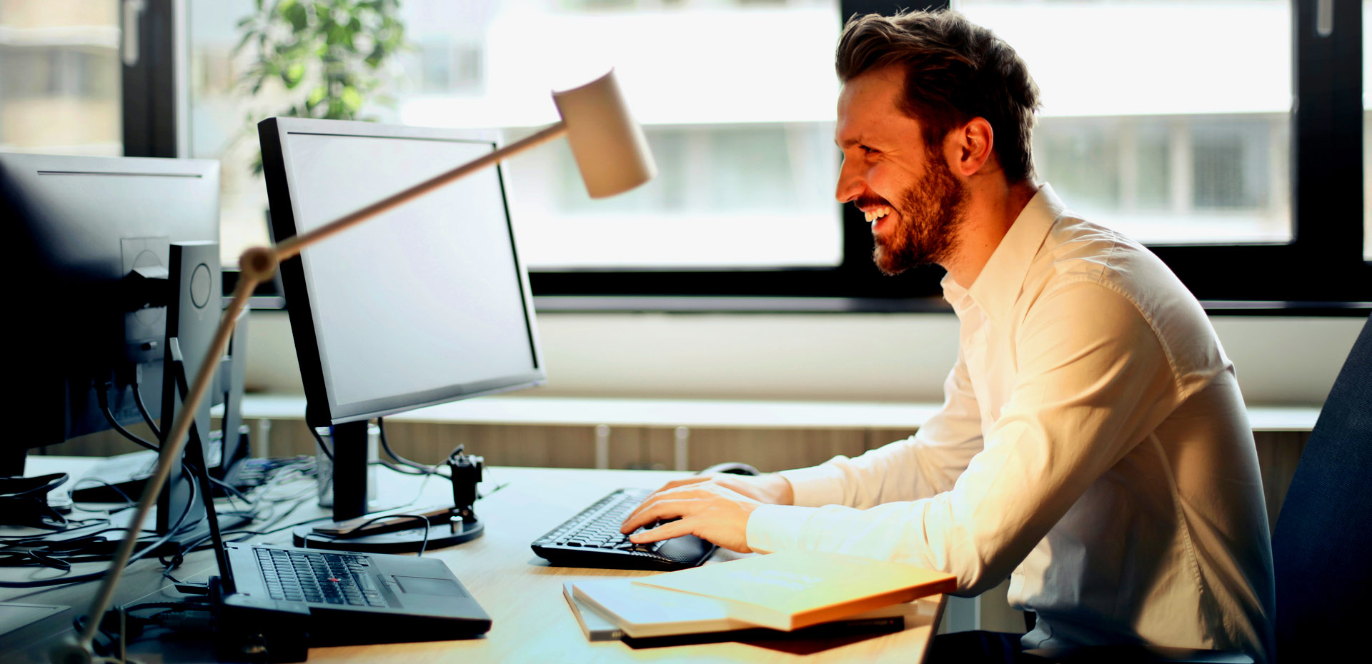 Imagen de un hombre de perfil sentado en su oficina mientras teclea sonriente en su computadora